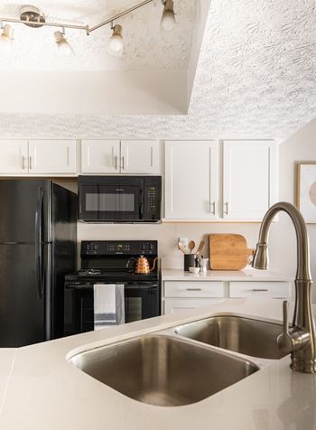 A modern kitchen with a black refrigerator and stove, white cabinets, and a stainless steel sink.